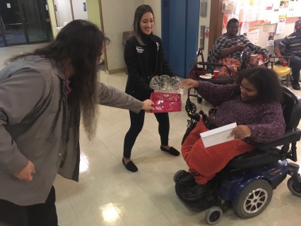 Two volunteers lean out to Chastity in a wheelchair so that she can draw her raffle ticket from the basket and claim her prize. 